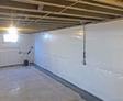 Unfinished basement with exposed ceiling beams and white plastic wall covering. Small window and sump pump visible.