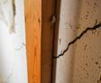 Close-up of a wall with a long, deep crack next to a wooden beam, indicating structural damage.