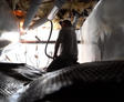 Person working in a dimly lit attic, surrounded by insulation and pipes, with light coming from behind.