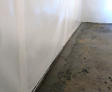 A basement with white walls and a concrete floor, featuring water damage along the edges.