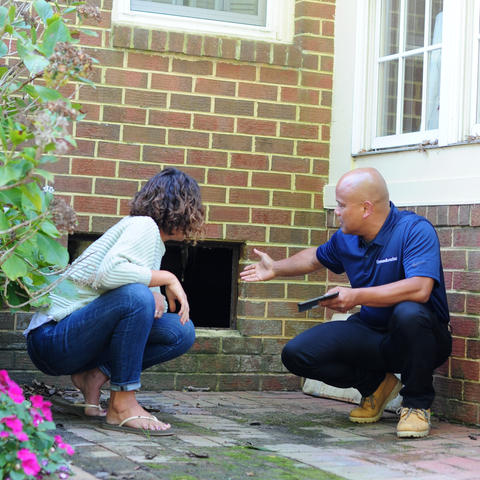 CFI speaking to homeowner while pointing at crawl space door opening.