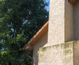 Stucco wall with rustic wooden trim, adjacent to green leafy trees under a clear blue sky.
