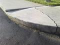 Cracked concrete sidewalk curb next to asphalt road and grass.