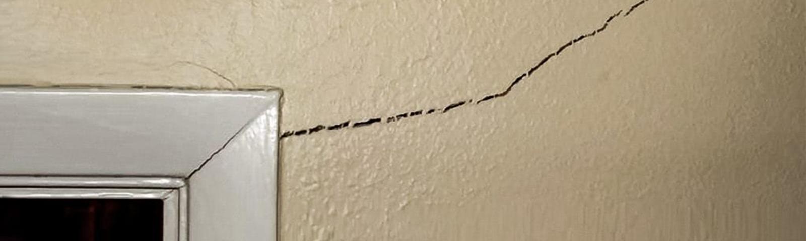 A diagonal crack on a beige interior wall above a white door frame.