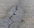 Close-up of a crack in a gray concrete surface, showing rough texture and irregular line.