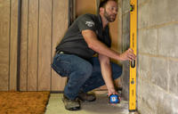 A man uses a level tool on a concrete wall in a room under construction.