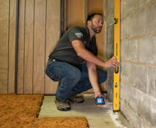 A man uses a level tool on a concrete wall in a room under construction.