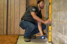 A man uses a level tool on a concrete wall in a room under construction.