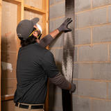 A person applying a black strip to a concrete wall in a construction setting, wearing protective gear.