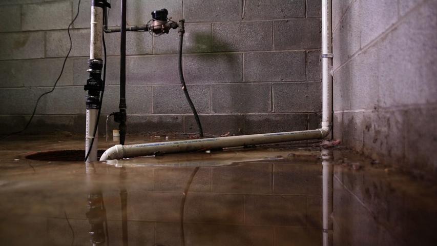 Flooded basement with water pipes and reflections on the wet floor.