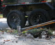 A person uses a sledgehammer to break concrete on a sidewalk near a trailer.