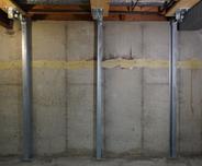 Basement wall with steel beams for structural support against concrete, showing a horizontal repair line.