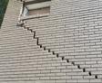 A brick wall with a zigzag crack extending downward from a small window.