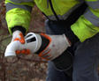 Person in a bright jacket and gloves handling a large hose with a white nozzle outdoors.