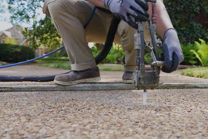 Person wearing gloves and boots operates equipment to level a concrete sidewalk.