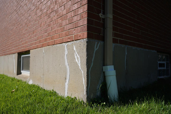 Red brick building corner with repaired concrete foundation and green grass.