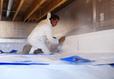 Person in protective suit installing insulation in a basement or crawl space.