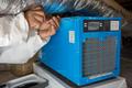 Person in protective gear repairing a blue HVAC unit with a screwdriver.