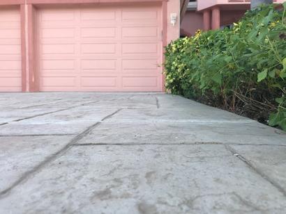 Close-up of a pink garage door with a stone driveway and green bushes on the right side.