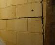 Close-up of a cracked, beige concrete block wall with shadowed lighting.