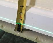 Tape measure against a wall with a green laser line, showing a height of 3 inches from the floor.