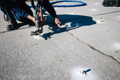 Person using equipment to inject material into cracks in concrete pavement.
