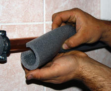 Hands are installing pipe insulation.