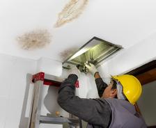 Technician repairing the pipe in the water-damaged ceiling.