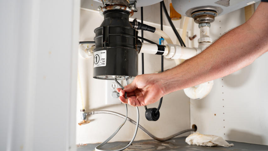 Hands are checking garbage disposal under sink.