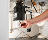 Hands are checking garbage disposal under sink.