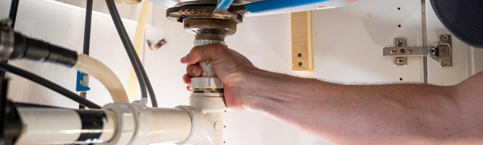 Hands tightening pipes under the sink with a wrench.