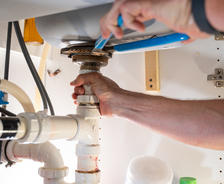 Hands tightening pipes under the sink with a wrench.