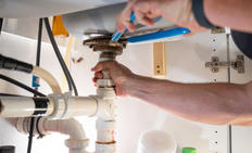 Hands tightening pipes under the sink with a wrench.