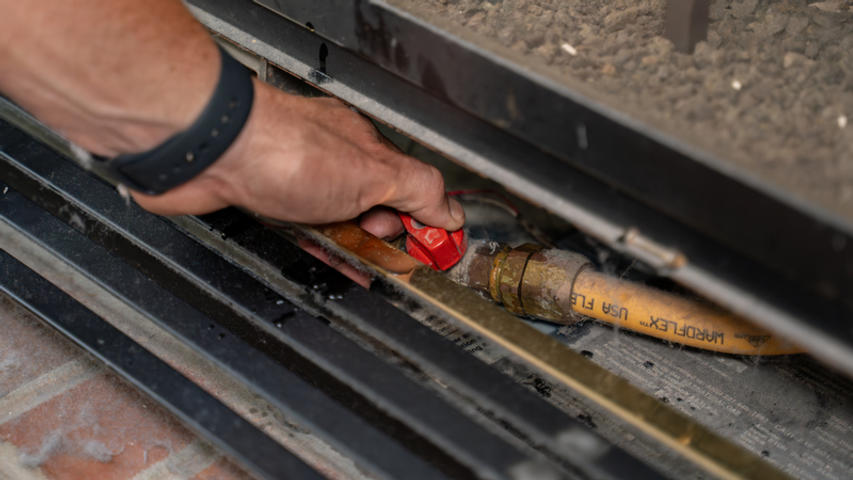 Hands holding gas line valve.