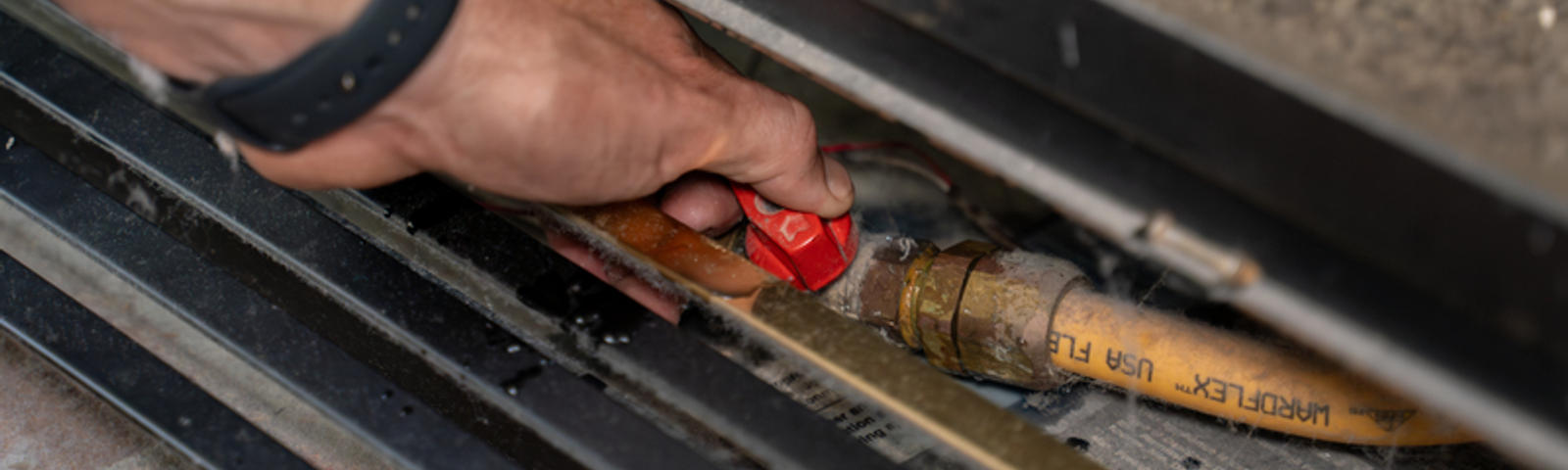 Hands holding gas line valve.