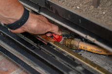 Hands holding gas line valve.