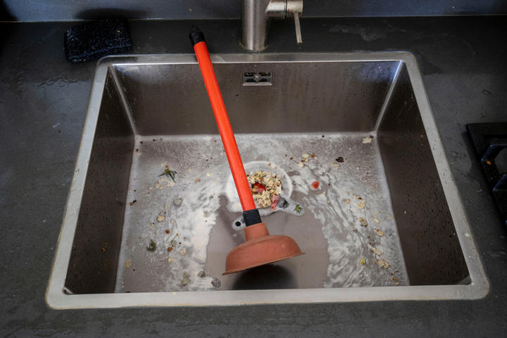 The plunger is sitting in the food-clogged kitchen sink.