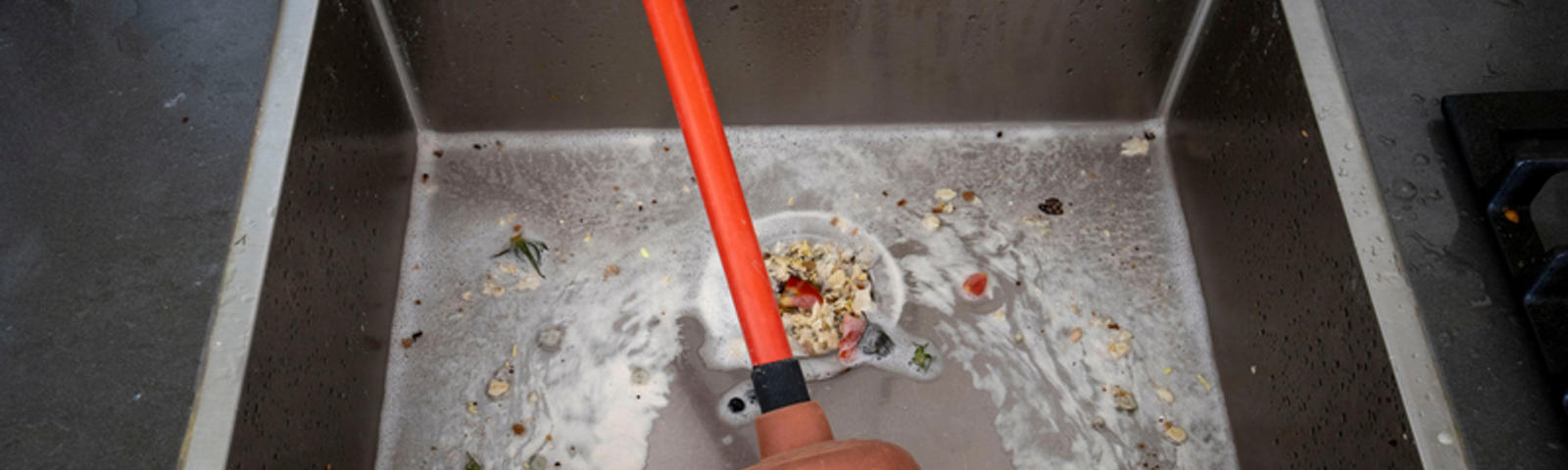 The plunger is sitting in the food-clogged kitchen sink.