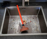 The plunger is sitting in the food-clogged kitchen sink.