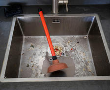 The plunger is sitting in the food-clogged kitchen sink.