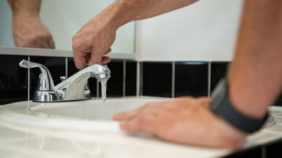 Hands turning on faucet in bathroom.