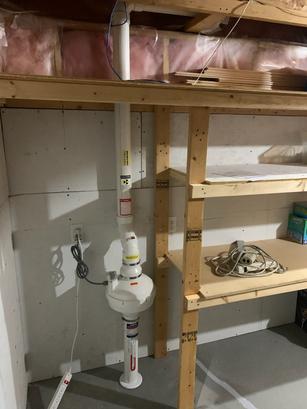 Radon mitigation system installed in a basement corner near wooden shelving.