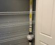 Empty wire shelves in a closet with a radon mitigation system installed on one side.