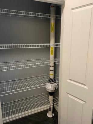 Empty wire shelves in a closet with a radon mitigation system installed on one side.