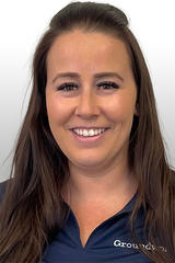 Smiling woman with long brown hair wearing a dark navy shirt, posed against a light gray background.