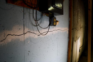 The basement wall shows a significant crack, raising concerns about horizontal vs. vertical wall cracks. Nearby, electrical wires and an outlet add to the attention needed for repairs.