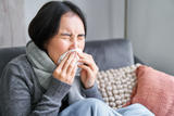 Wrapped in a cozy scarf on the couch, a person sneezes into a tissue, pondering if their persistent sniffles are due to allergens. Thoughts drift to practical solutions like addressing how to remove crawl space mold that might be contributing to the constant sneezing.