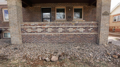 A brick house with a front porch, surrounded by gravel and rocks.
