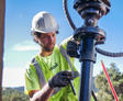 Worker in safety gear operating machinery outdoors on a sunny day.
