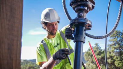 Worker in safety gear operating machinery outdoors on a sunny day.